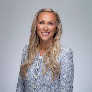 Shannon Laymon-Pecoraro with long blonde hair in a blue textured blazer smiling against a neutral background.