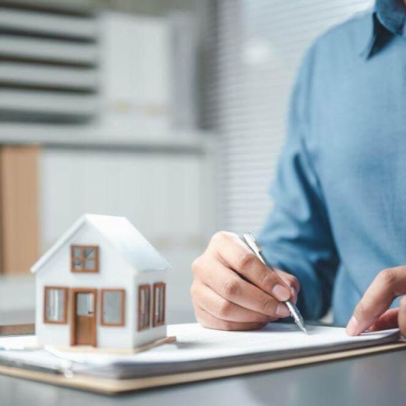 a man writing on a notepad with a model of a house
