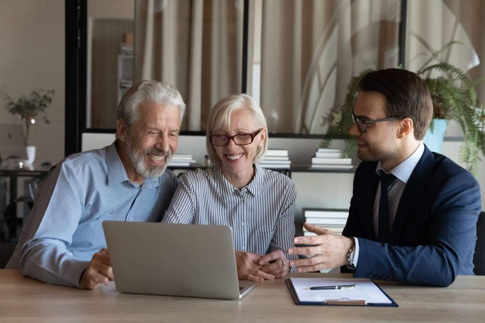 An elderly couple reviews something on a laptop with a lawyer