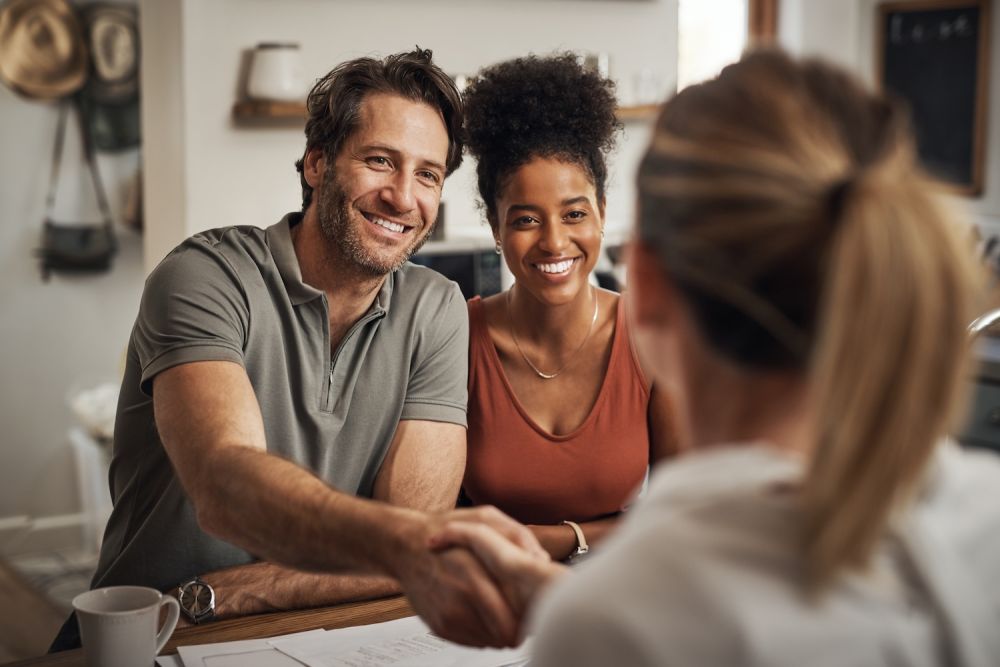 Smiling couple meeting with a professional, shaking hands across a table in a cozy office setting.