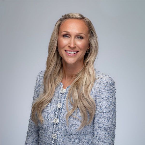 Shannon Laymon-Pecoraro with long blonde hair in a blue textured blazer smiling against a neutral background.