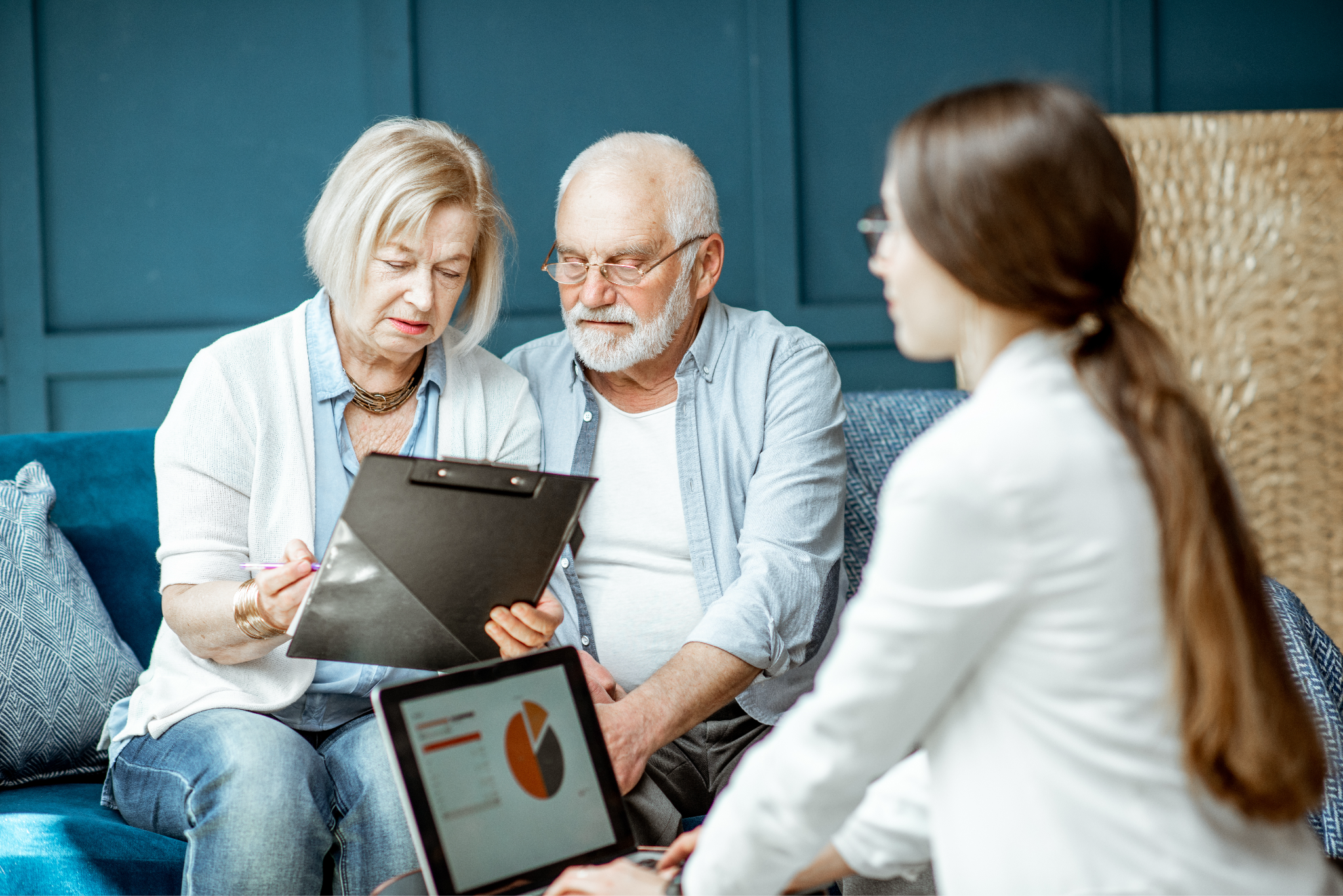 an elderly man and a woman sitting on a couch looking at something on a clipboard presented by a doctor