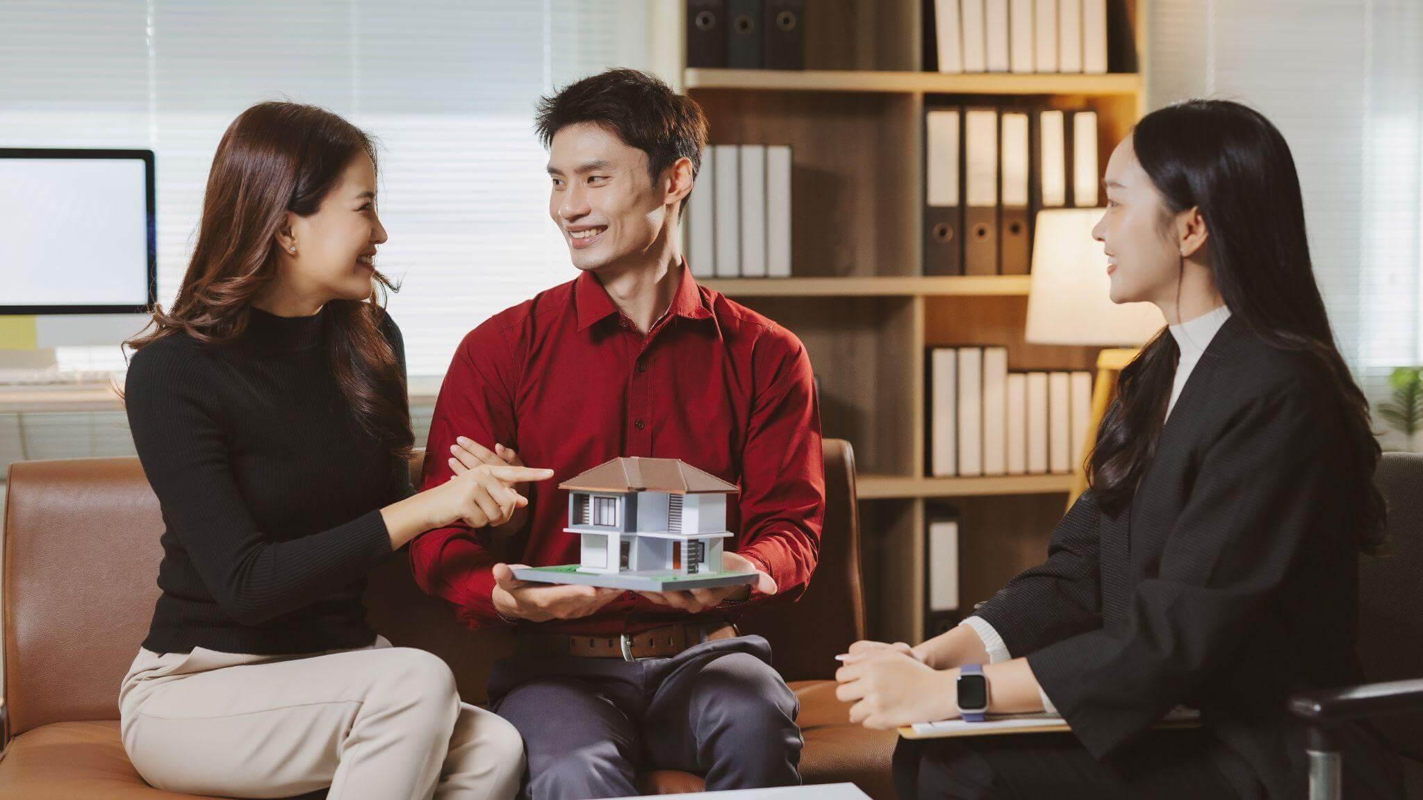 Three people holding a model house, symbolizing